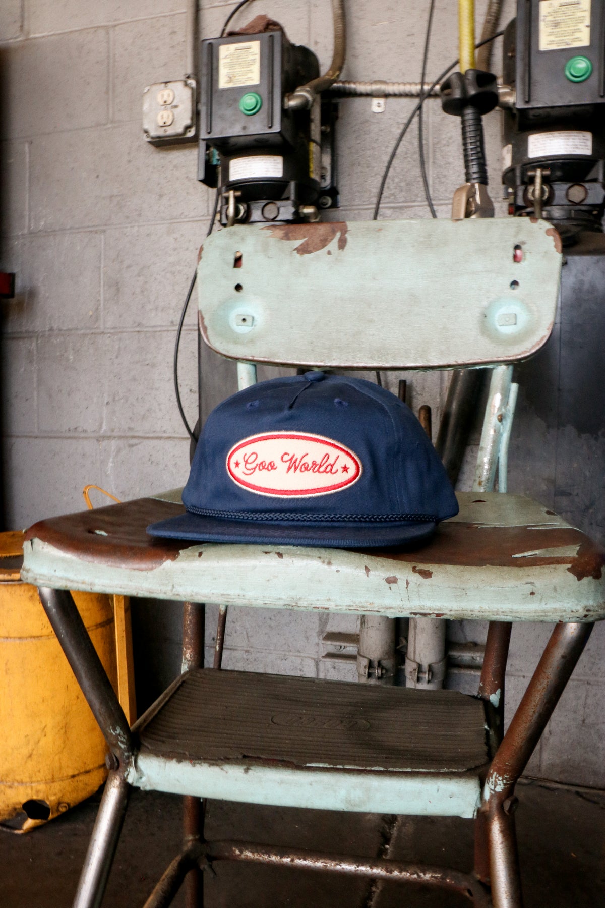 Navy GOO WORLD Mechanic's Hat on a rusty metal chair in an auto shop